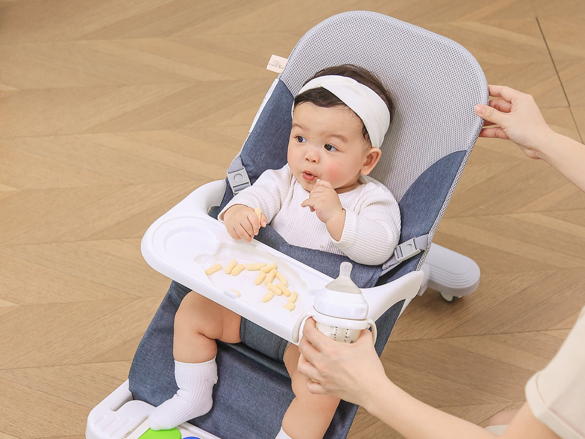 Parent feeding infant in Montessori baby bouncer chair during Snack Time